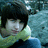 Pixelated static image of a person with dark hair and light skin wearing green clothing against a blue background.