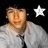 Pixelated image of a person in a light gray shirt and dark tie with a white star symbol on a black background.