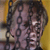 Pixelated image of a person with dark hair and light skin, wearing a dark top against a yellow background with blurred vertical elements.
