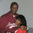 Two people in close physical proximity; one wears a maroon shirt with white graphic, the other red clothing. Background is light gray.