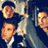 Pixelated static image of three stylized human faces with orange-brown skin tones against a dark blue background, featuring visible dithering and low-resolution rendering artifacts.