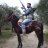 Pixelated image of a person riding a dark horse, raising one arm upward against a blurred outdoor background.