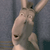 A pixelated animal figure with light brown fur, dark eyes, and a small nose, positioned against a gray background with a blurred vertical element.