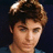 Pixelated close-up of a person with light brown hair styled in a voluminous, swept-back manner against a dark background.