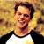 Static pixelated image of a person with short dark hair wearing a black and white raglan shirt against a yellowish-brown background.