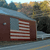 A pixelated image shows a building with an American flag on its side, set against a blurred background of trees and sky.