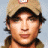 A pixelated image of a person wearing a beige cap with dark brim and light brown hair, next to green text on dark background.