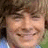 Pixelated close-up of a smiling person with light skin, brown hair, and closed eyes against a blurred background.