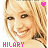 Pixelated image of a smiling person with blonde hair, pink text reading HILARY below, and a small pink heart symbol in the top right corner.