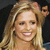 Pixelated close-up of a smiling person with long blonde hair against dark background.