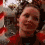 A person with curly brown hair wears a red and black top, smiling in a sequence of four pixelated frames showing slight head and mouth movement.