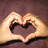 Two hands forming a heart shape against a dark brown background with pixelated texture.