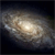 A static pixelated image of a spiral galaxy with a bright central core and fainter outer arms against a dark background.