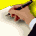 A hand writes on paper with a pen, showing motion from initial stroke to completed text against yellow and white background.