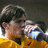Pixelated image of a person with dark hair wearing a yellow garment, holding a blue and white object against a dark background.