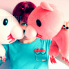A person in a teal shirt holds two plush toys: a white rabbit and a pink pig, with a blurred background.