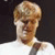 Pixelated close-up of a person with light brown hair wearing a white shirt against a dark background.