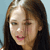 A pixelated close-up of a person with long brown hair, light skin, and a black top against a light blue background.