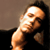 Pixelated static image of a person with dark hair and light skin leaning against a wall, wearing a black top with visible shoulder strap.
