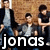 A static image of four young men in casual clothing against a brick wall background with text overlay.