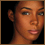 Pixelated close-up of a person's face with brown skin tone, visible ear, and neutral expression against black background.
