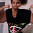 A person in a black top with green and white patterns holds an object near their face against a light background.