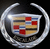 A circular silver emblem with a central shield divided into red, blue, and gold sections on black background.