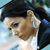 Pixelated static image of a person's face with dark hair and light skin, wearing a white shirt under a dark jacket against a blurred background.