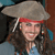 A pixelated figure with long dark hair wears a wide-brimmed gray hat and red headband, smiling with visible teeth against a blurred background.