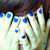 A person with dark brown hair covers their face with both hands, showing blue-painted fingernails and a red mouth.