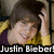 A person with brown hair wearing a yellow jacket over a dark purple shirt, smiling and touching their head in