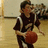 Pixelated image of a person holding a basketball, wearing dark clothing with light stripes on sleeves and pants.