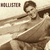 Pixelated image of a person with short brown hair wearing a sleeveless top, standing against a light background with horizontal lines.