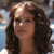 A pixelated close-up of a person with long dark brown hair, light skin, and a neutral expression against a blurred background.