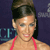 Pixelated image of a person with dark hair in an updo wearing a pink strap top against a dark blue background with partial light blue text.