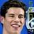 Pixelated close-up of a smiling person with dark hair against a blue background, partially showing a white and black object on the right.