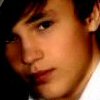 A close-up of a person's face with dark hair, wearing a white shirt and partially visible dark jacket.