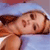A pixelated image shows a person lying on their back with eyes closed, wearing a light blue cap and light blue clothing against a blurred background.