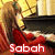 A pixelated image of a woman with long brown hair in a red dress, seated at a table with a golden background, with the text 'Sabah' in white at the bottom.