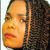 A pixelated close-up of a person's face with dark curly hair, orange-toned skin, and red lips, set against a light background.