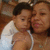 A woman and child in white tank tops pose closely together, the woman's arm around the child, with a blurred background.