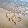 Two interlocking heart shapes drawn in wet sand on a beach, with gentle waves lapping at the shore in the background.