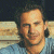 A pixelated image of a person with dark hair and light skin wearing a blue shirt, positioned next to green text reading 'Original Icons .com' on a solid background.