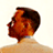 Pixelated static image of a person's head and shoulders in profile view with warm orange-brown tones against a light background.