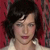 A pixelated portrait of a person with short dark hair against a red background, wearing a light-colored top.
