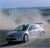 A pixelated static image shows a dark blue car on a light gray road with a blurred background of sky and distant shapes.