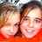 Two pixelated faces in close-up, one with light skin and brown hair, the other with lighter skin and dark hair, both smiling against a red background.
