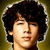 Pixelated close-up of a person with dark curly hair against a yellowish-brown background, eyes closed, mouth slightly open.