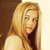 A static pixelated image of a person with long blonde hair wearing a light-colored top against a dark brown and beige background.
