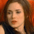Pixelated close-up of a person with brown hair wearing a dark top against a warm-toned background.